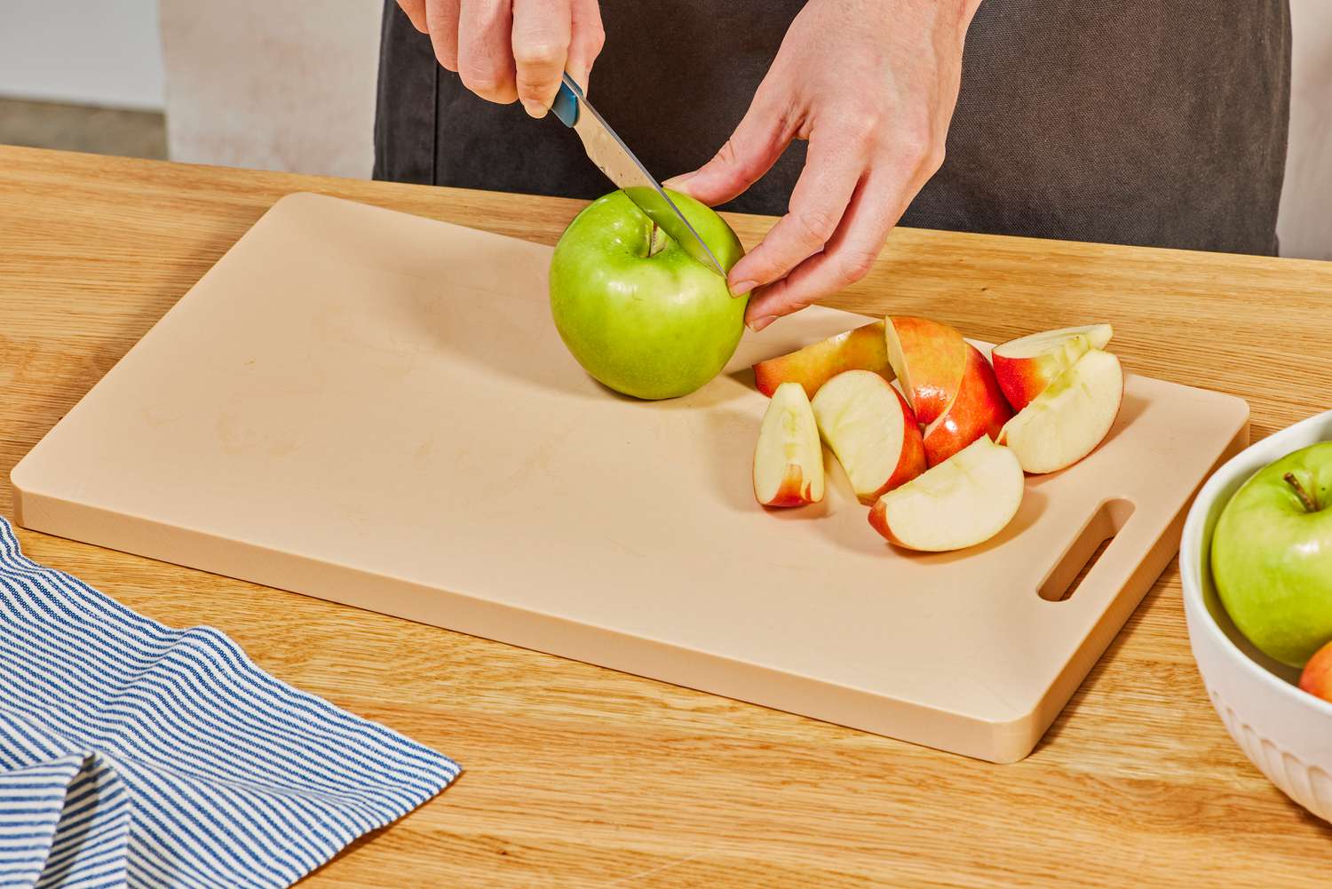 A person slicing apples on a plastic cutting board.