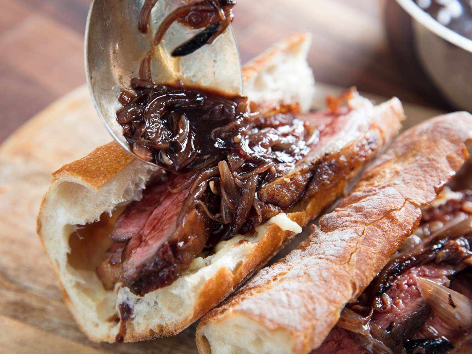 Spooning shallot jus over roast beef sandwiches.