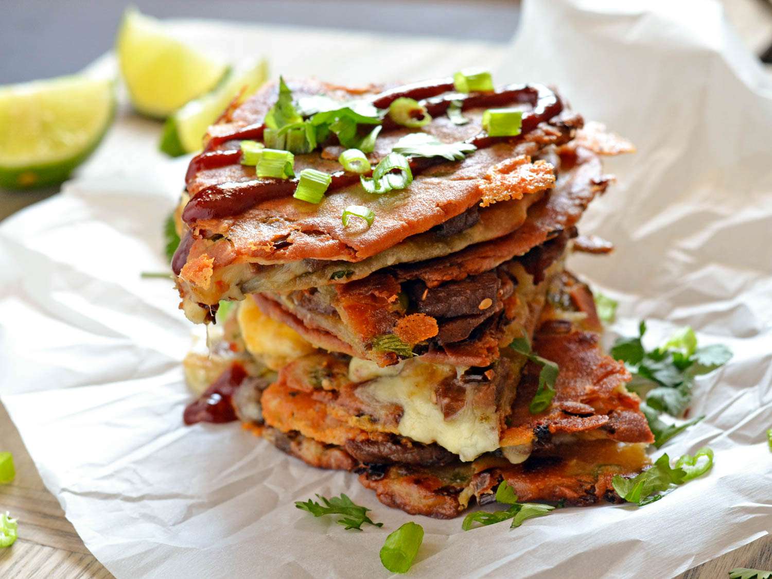 A finished bulgogi scallion pancake-adilla has been quartered, stacked high, and garnished with green onion and gochujang.