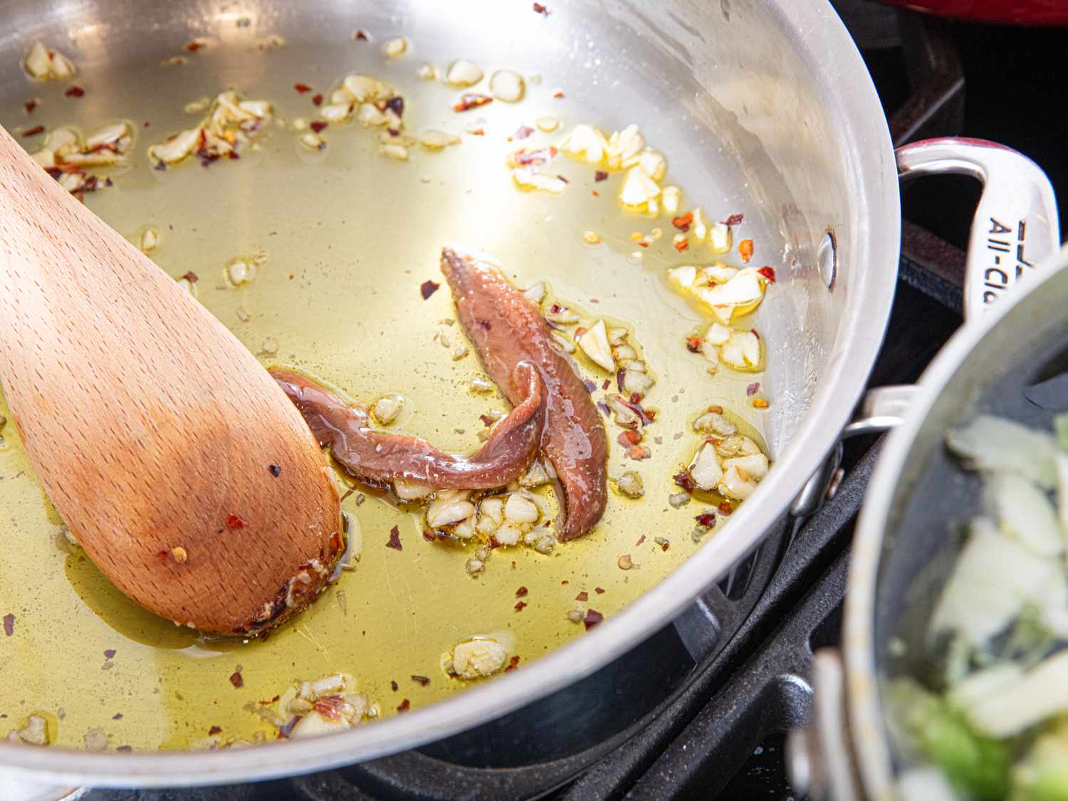 Wooden spatula stirring garlic oil and anchovies in a skillet