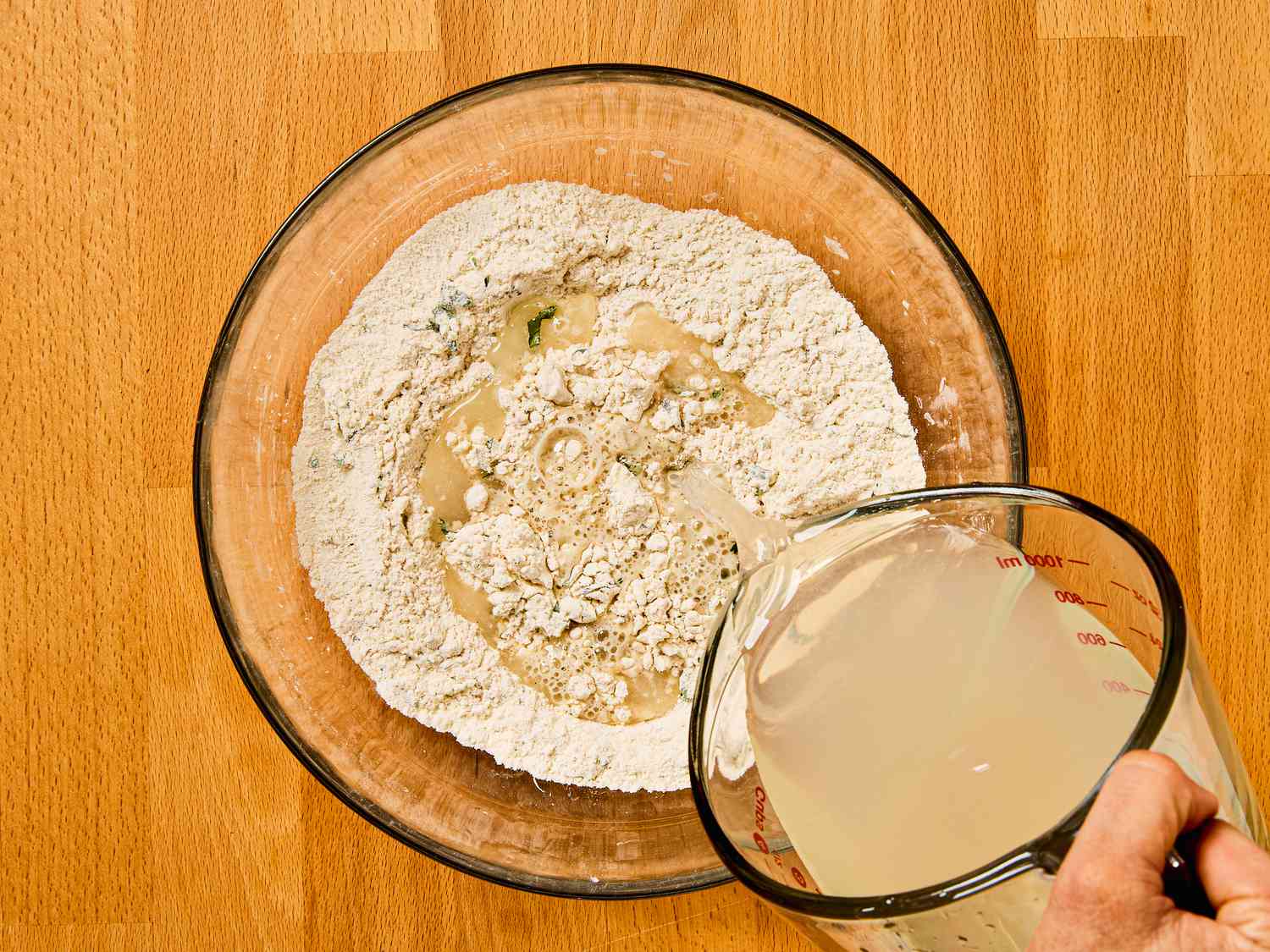 Mixing batter together with bacalao water from a measuring cup to a glass bowl 