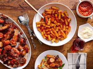 Overhead view of a tablescape of RagÃº Napoletano with pasta, a single serving, the platter of meat, extra sauce and extra cheese