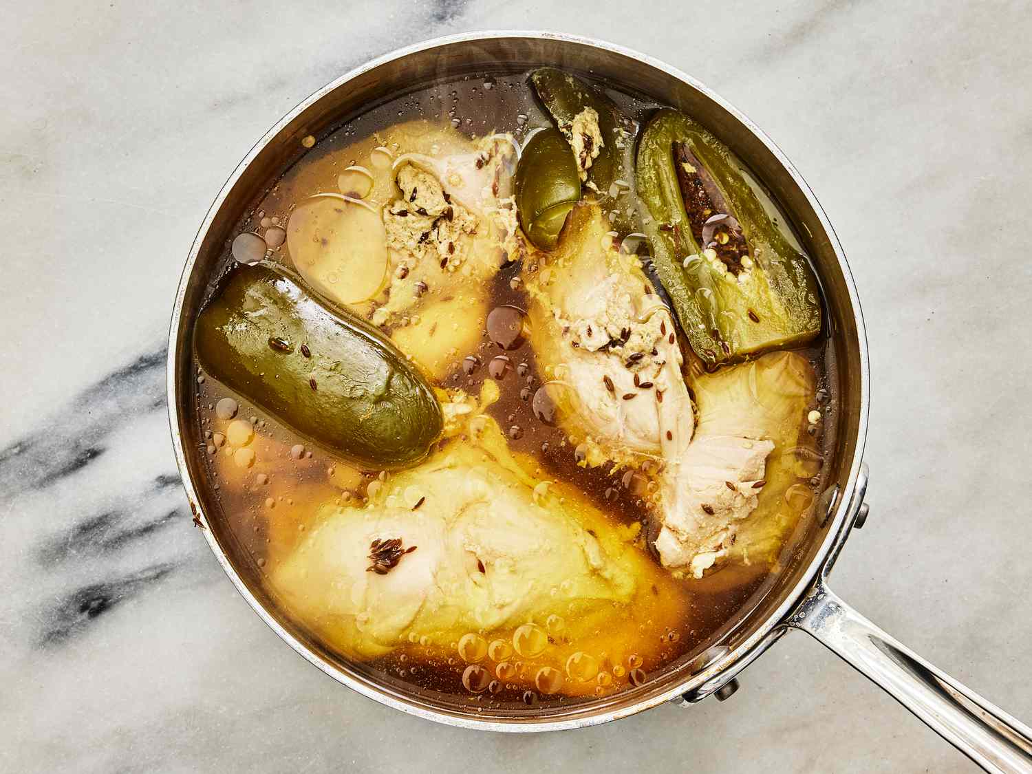chicken and peppers poaching in a pot on a white marble surface 