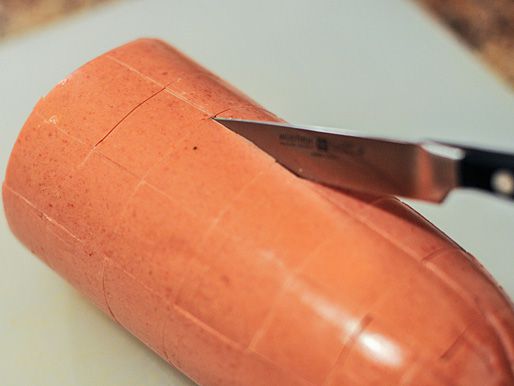 A log of bologna, being scored in a grid pattern with a paring knife.