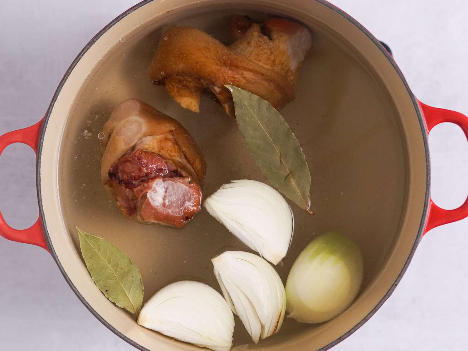 Two ham hocks, bay leaves, a quartered onion, and water in a Dutch oven.
