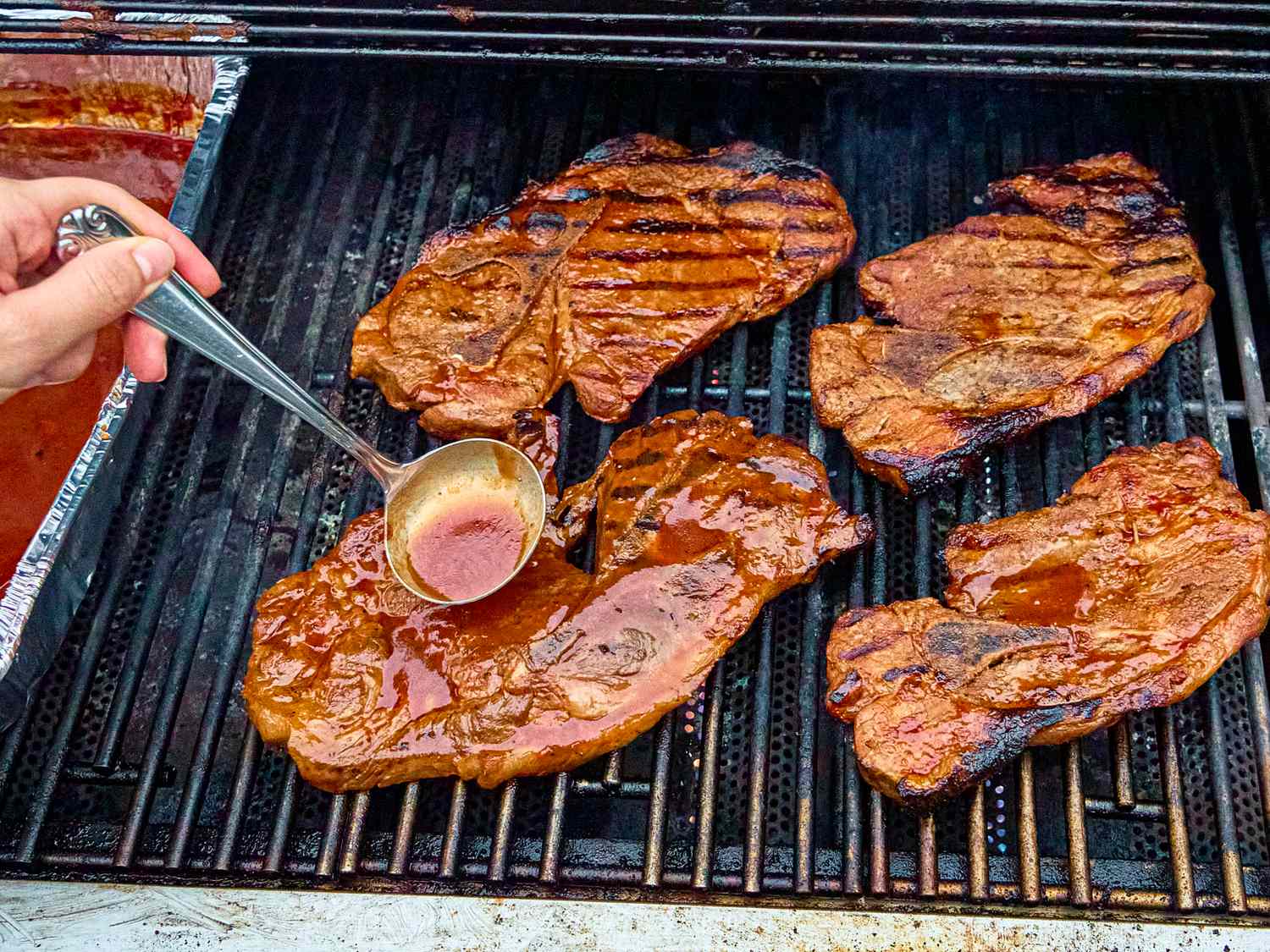 Grilling pork steaks being basted with sauce on a barbecue grill