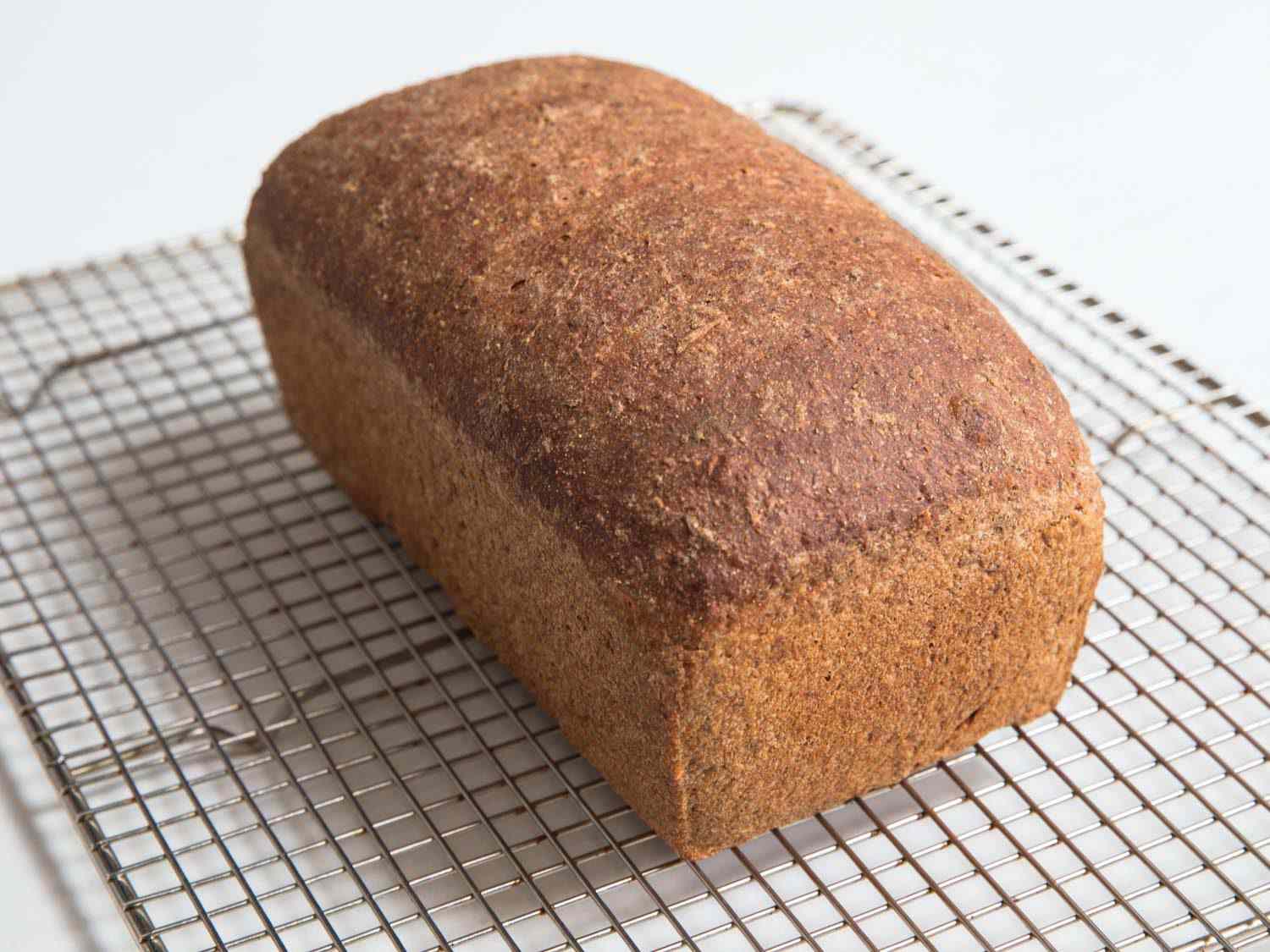A loaf of multigrain bread cooling on a wire rack