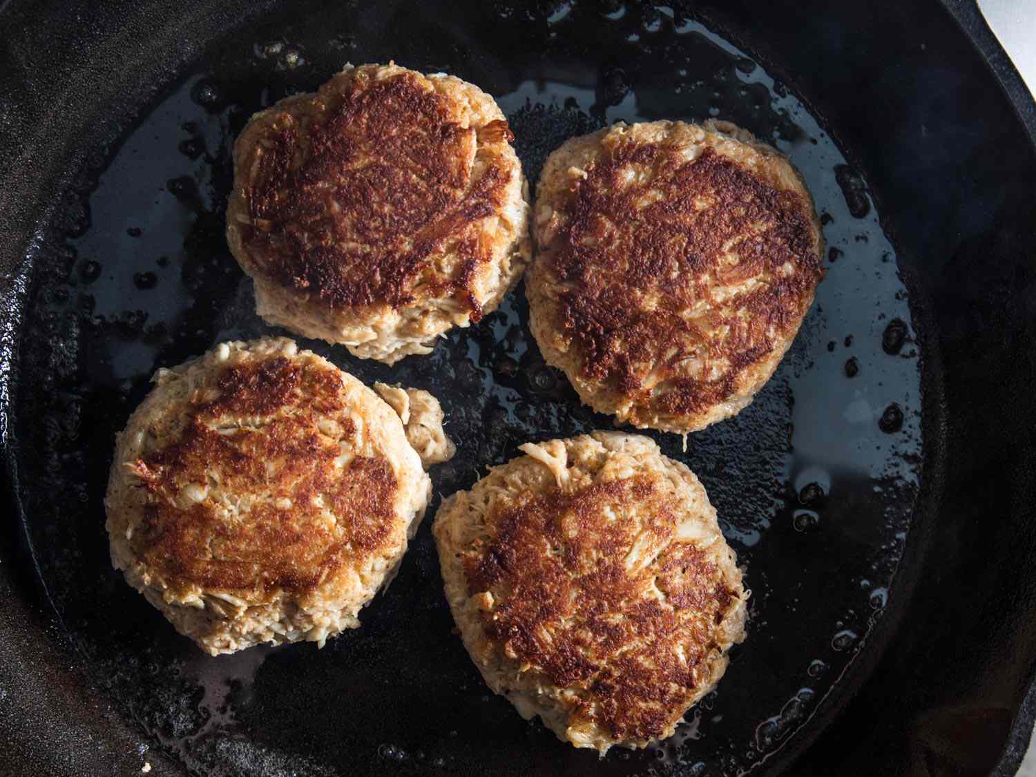 Overhead view of Maryland crab cakes cooking in a cast iron skillet.