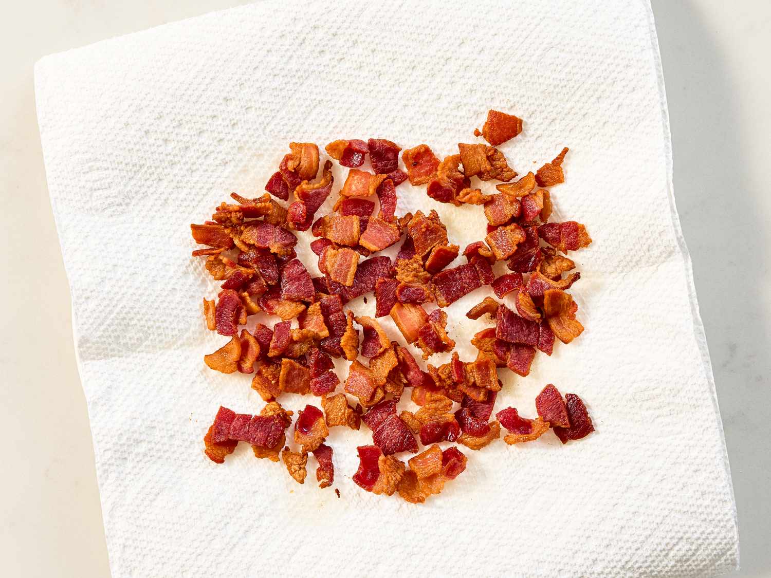 Crisped and crumbled pieces of bacon resting on a white paper towel