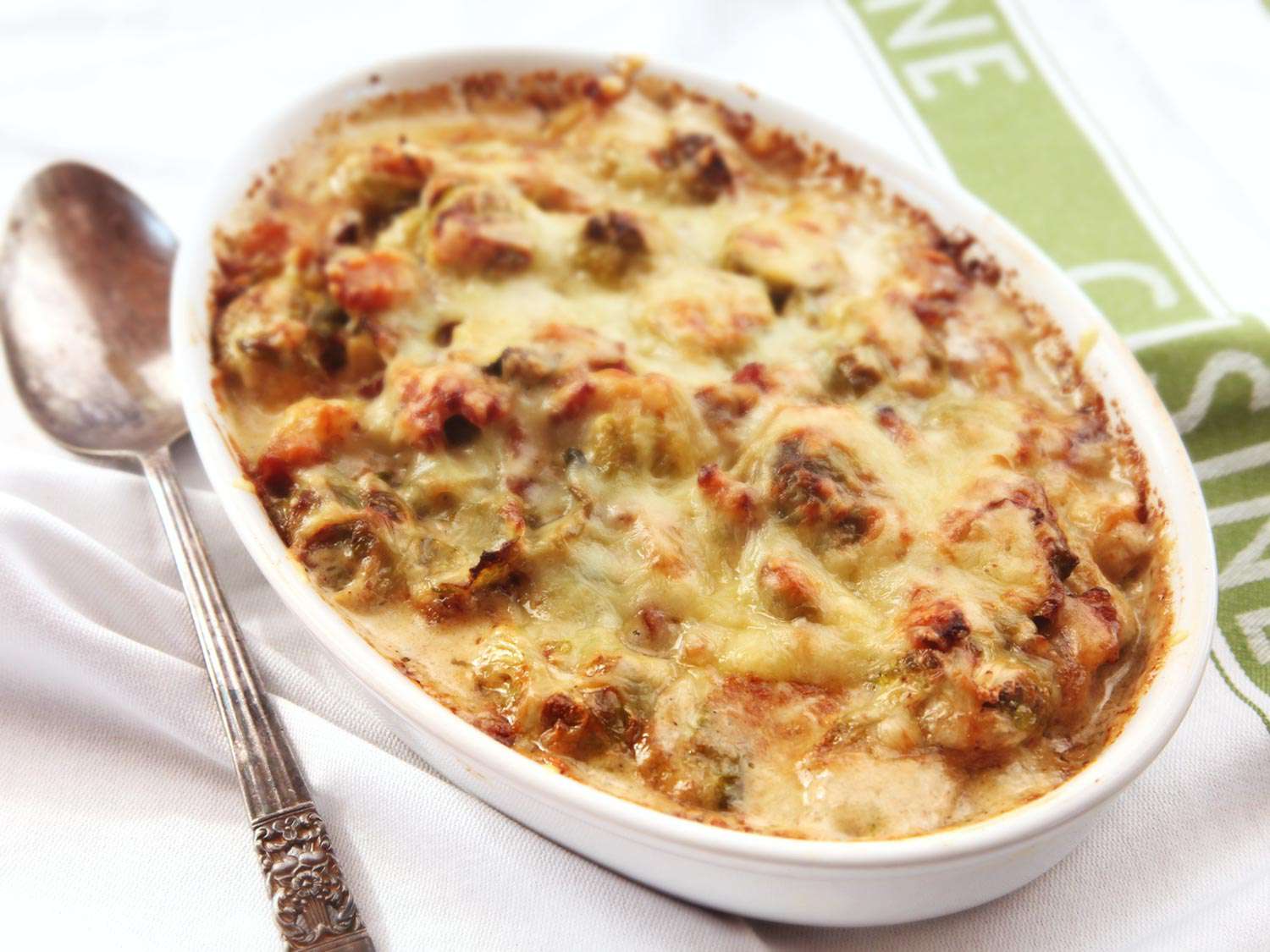 Brussels sprouts gratin with a crisp cheese crust in a casserole dish with a spoon alongside