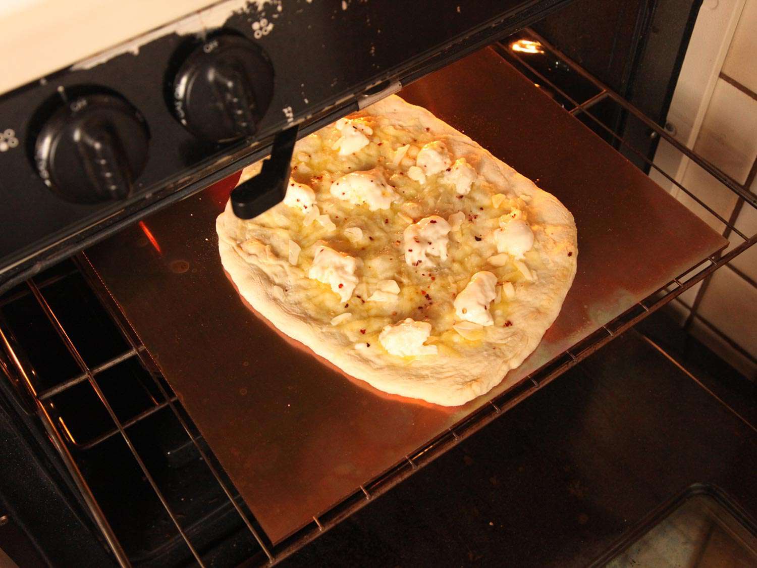 A pizza dough topped with torn mozzarella and shredded Gruyère on a baking steel about to go into the oven. 