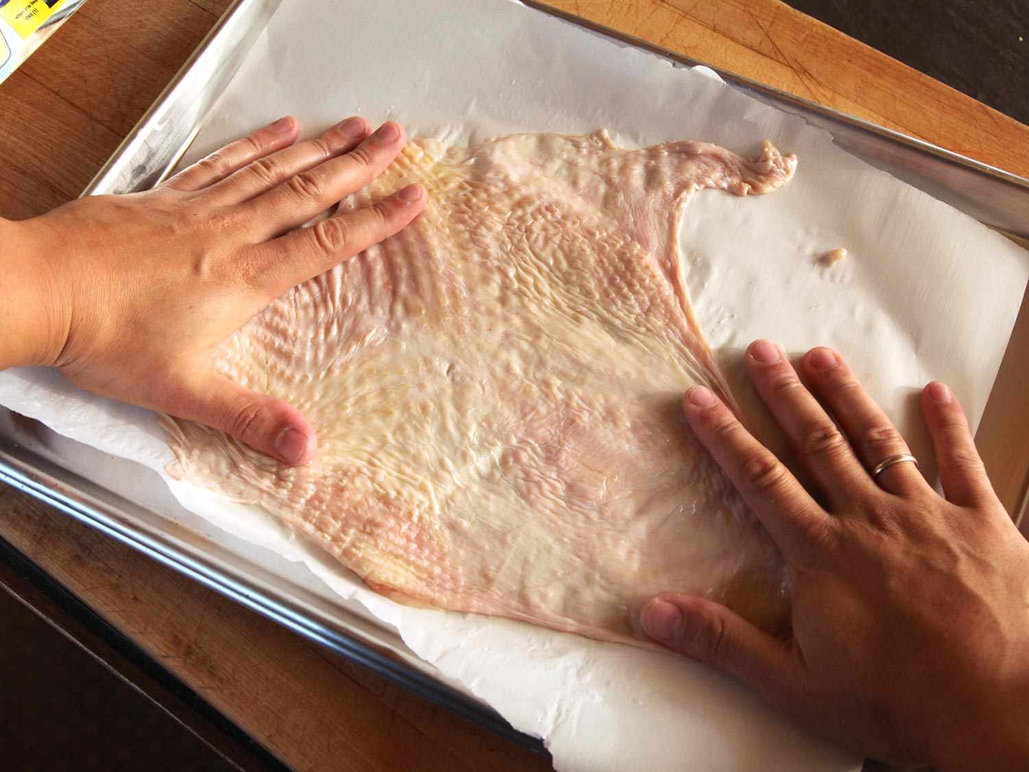 Using hands to spread raw turkey breast skin on a parchment-lined baking sheet before roasting.