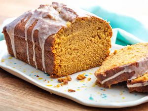A loaf of pumpkin bread topped with glaze on a tray. A few slices are on the tray next to the loaf.