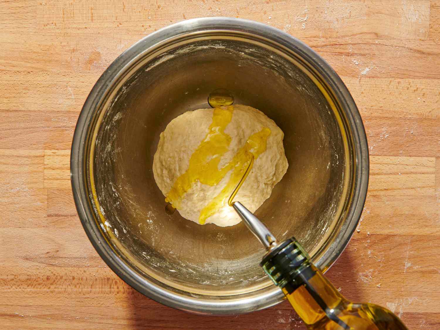 Phyllo dough in a metal bowl with olive oil being added