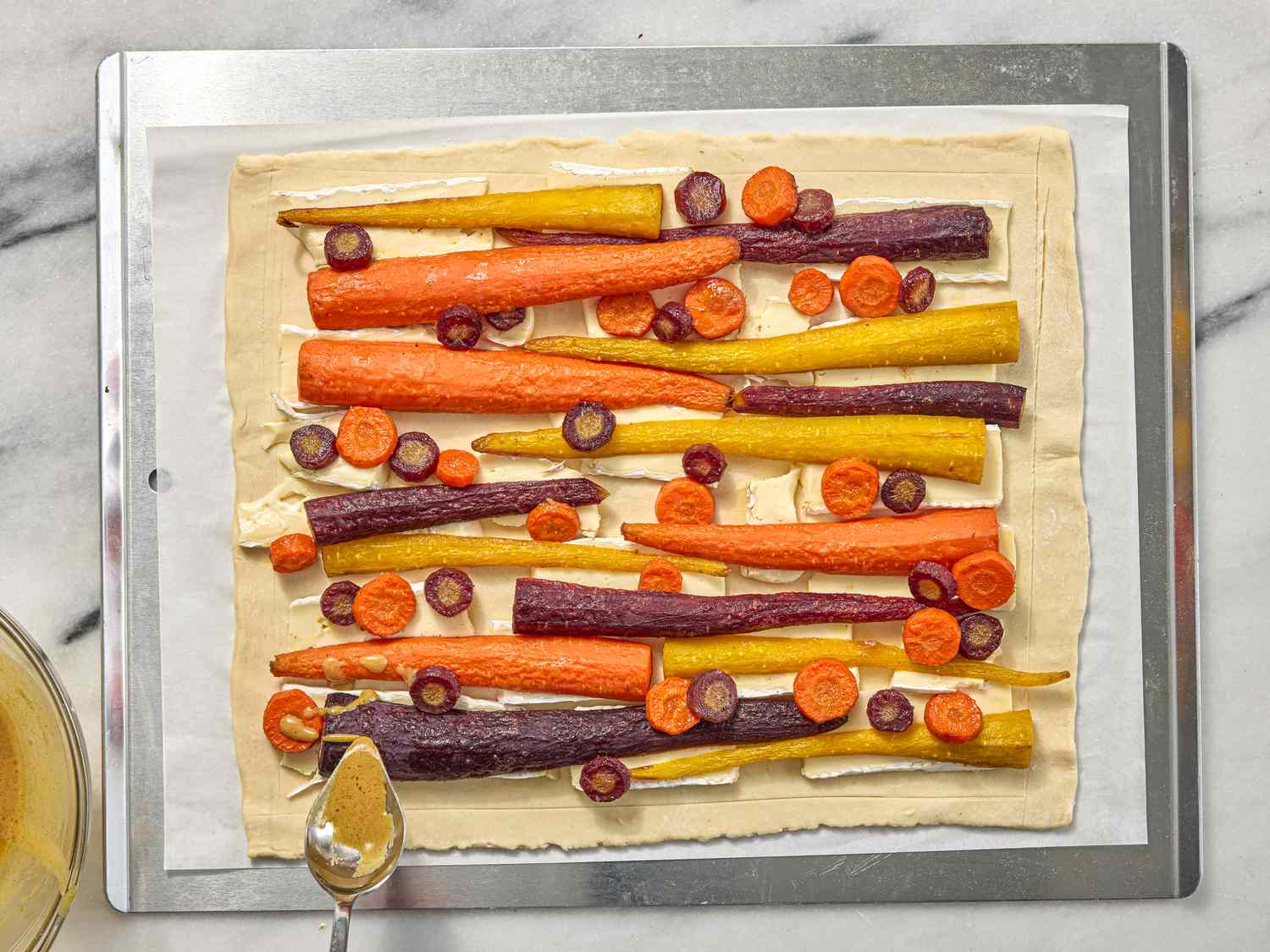 spooning honey on a carrot tart on a sheetpan 