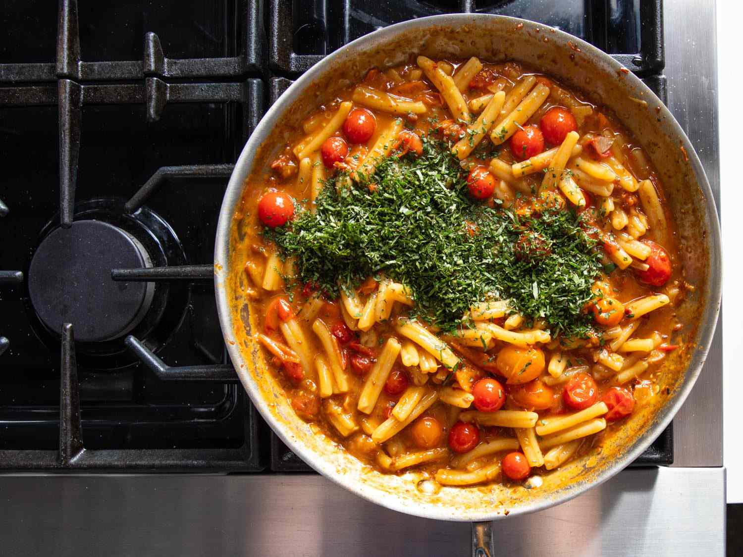 Chopped mint and basil added to skillet with pasta with burst cherry tomatoes and XO sauce.
