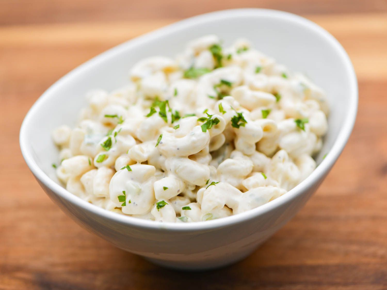 A small white bowl with macaroni salad, sprinkled with parsley.