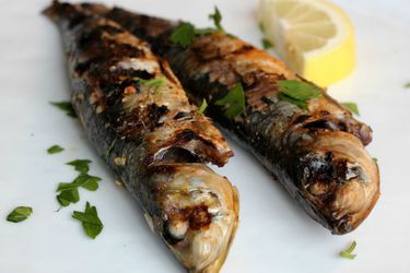 Grilled sardines seasoned with lemon, parsley, garlic, and paprika on a white plate. 
