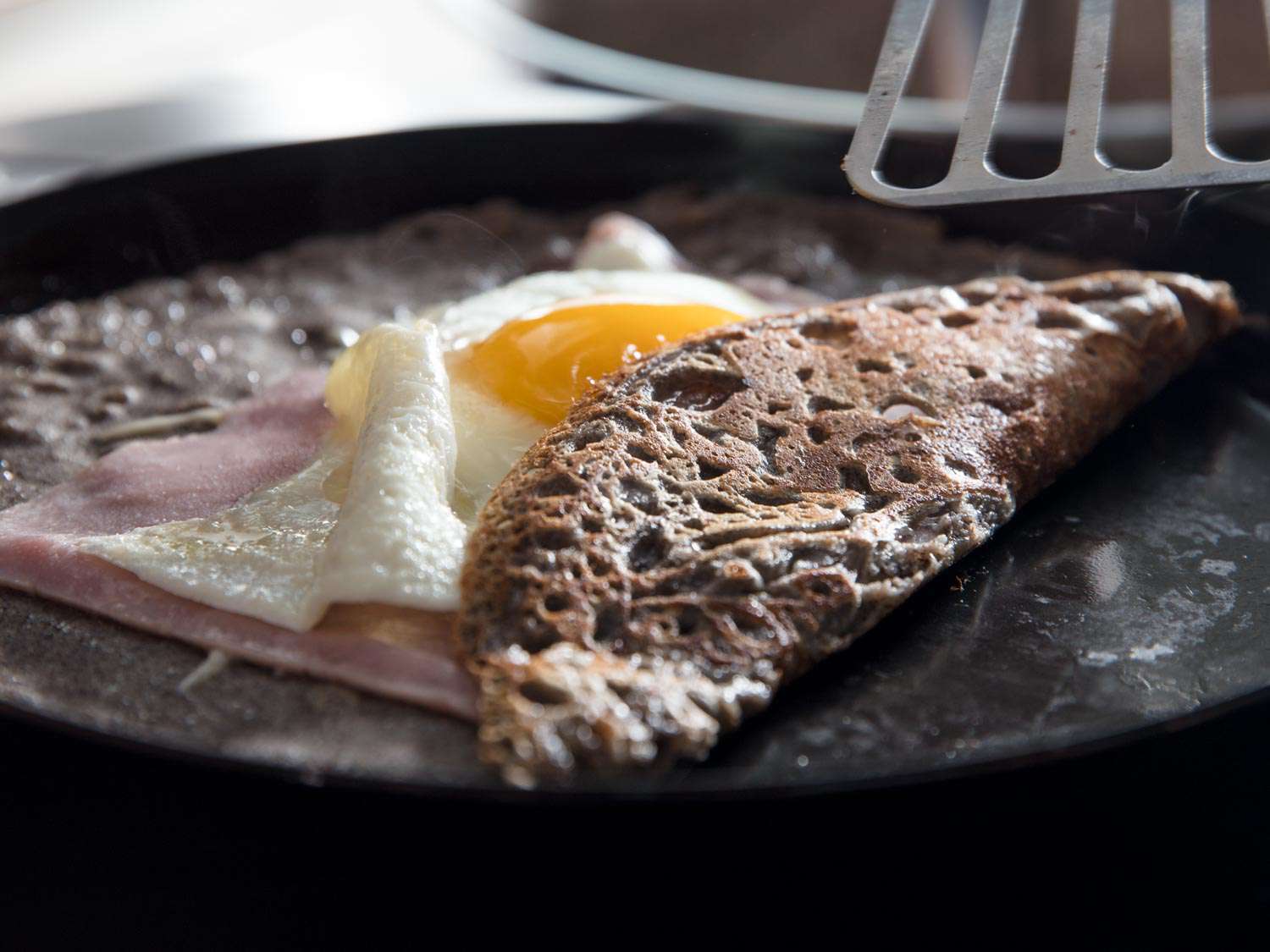 Close-up of one edge of a crepe being folded over onto the fillings of egg and ham.