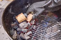 A hand adding wood chips on top of coals in the Weber Original Kettle Premium 22-Inch Charcoal Grill