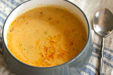 A bowl of beer cheese soup with bratwurst next to a spoon.