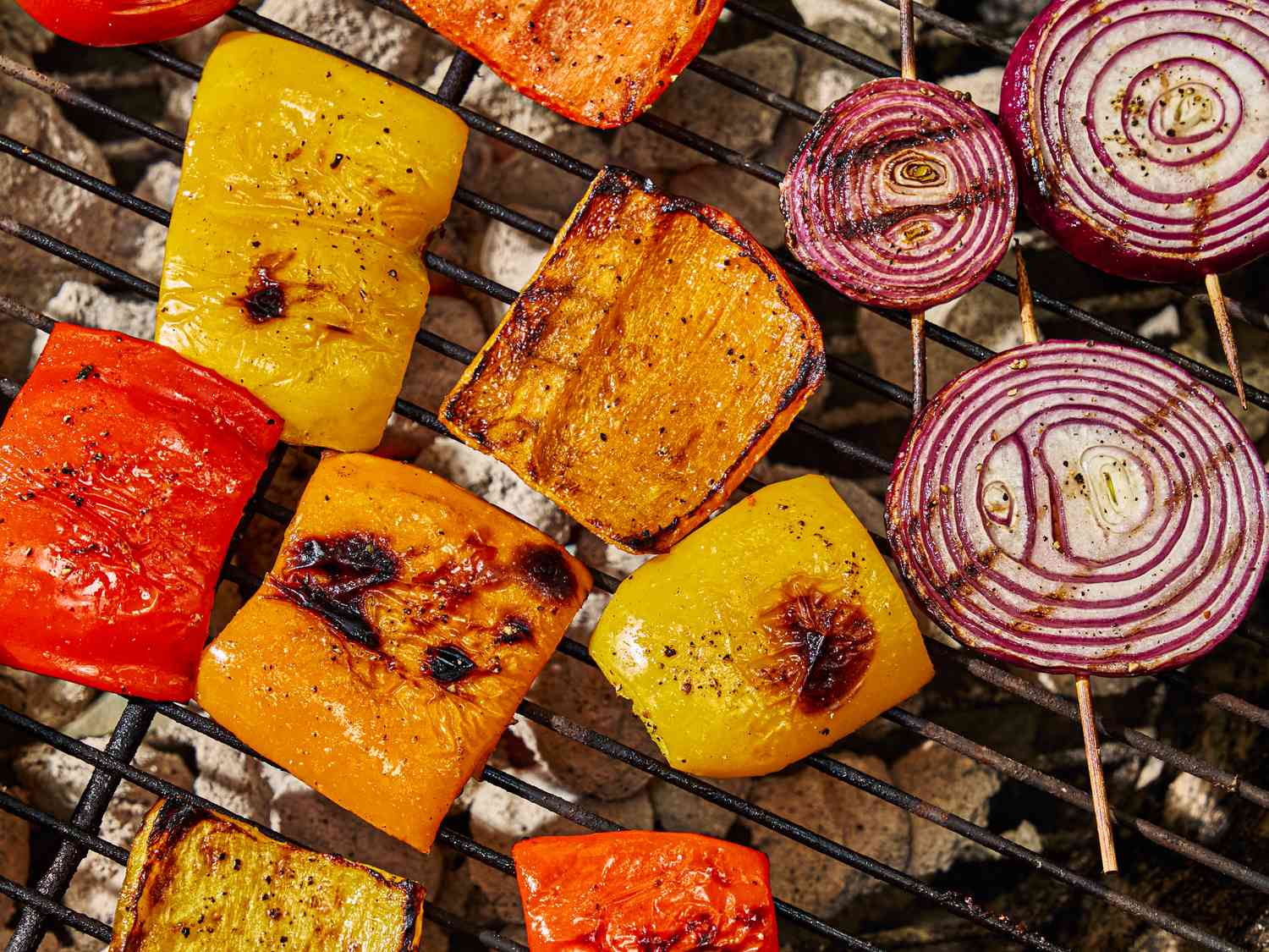 Grilled vegetable slices including bell peppers and red onions on a grill