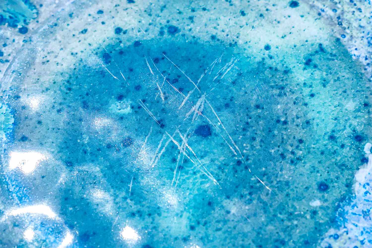 Closeup view of a textured Certified International Radiance Teal Melamine Dinnerware Set with blue patterns and white scratches