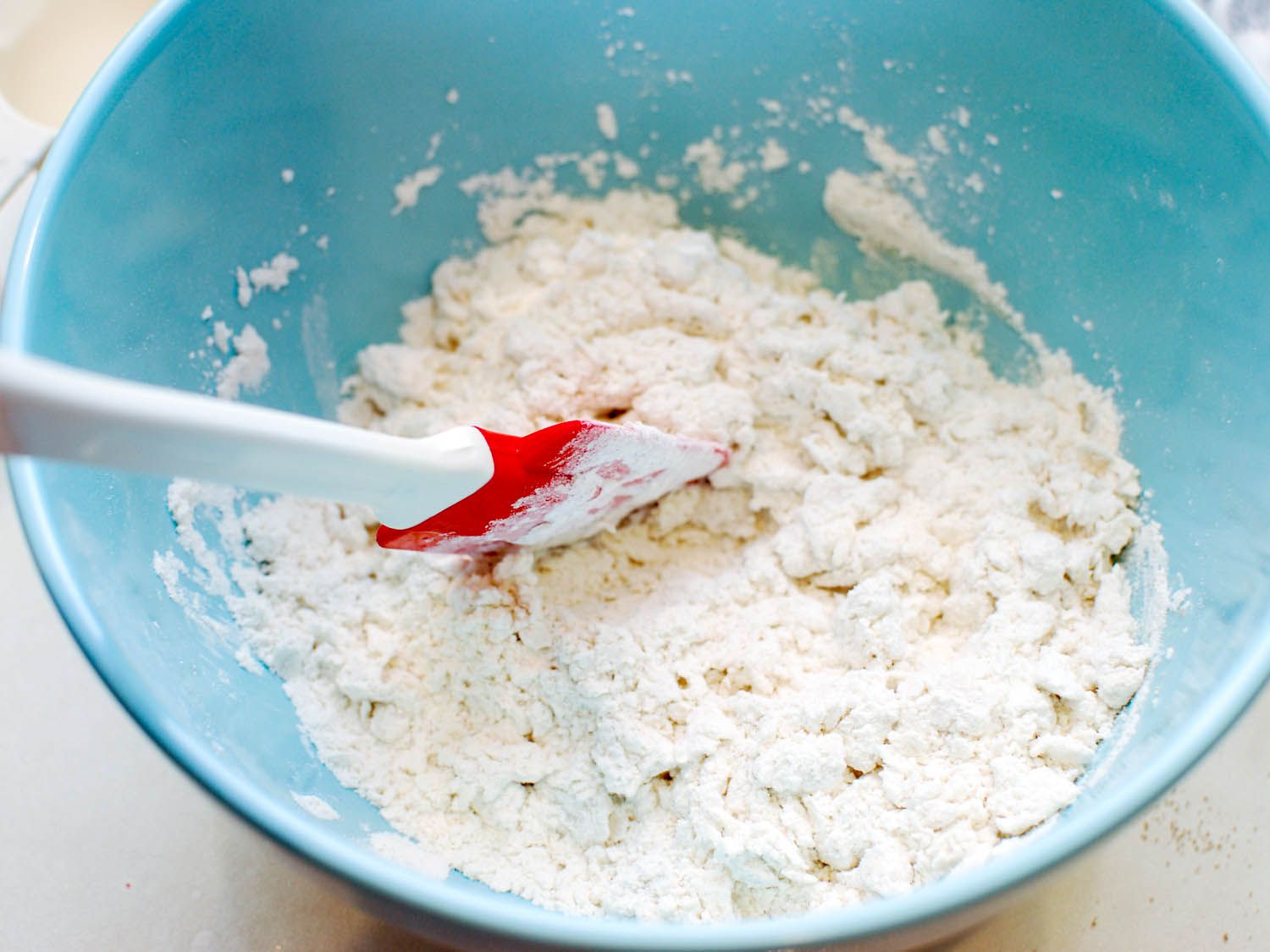 Warmed milk is mixed into the dry ingredients of the sheng jian bao dough with a flexible spatula.