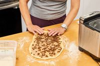 A person kneading dough containing raisins on a wooden counter to place into the Cuisinart CBK-110 Compact Automatic Bread Maker