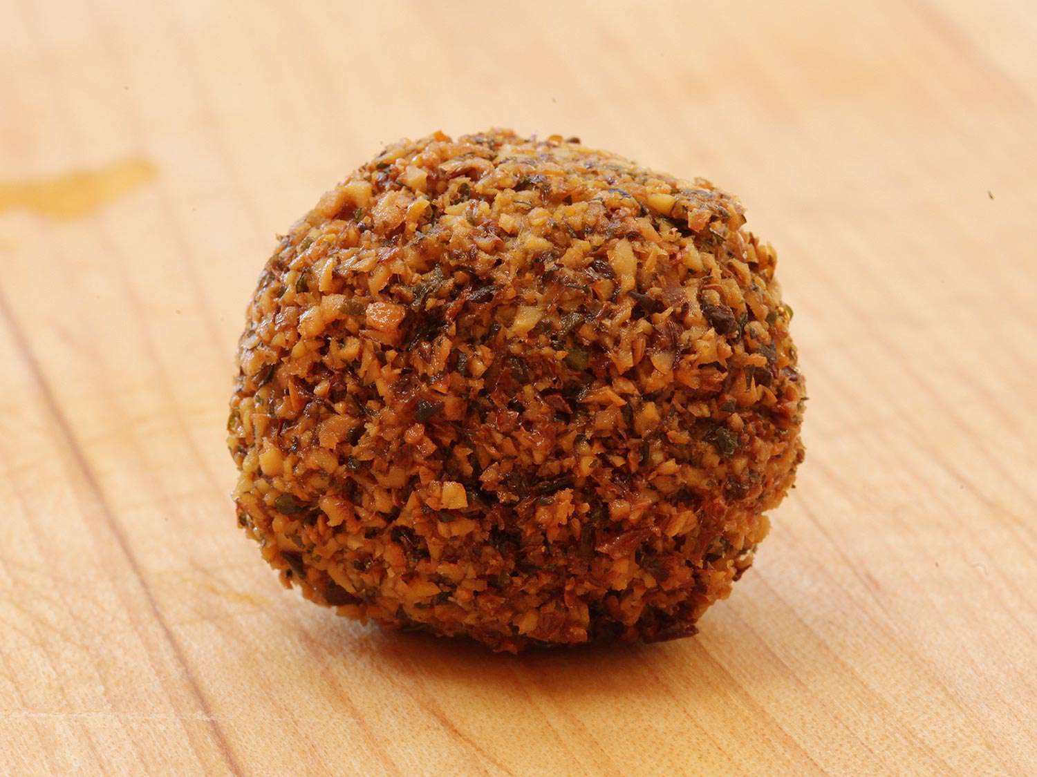 A crisp, golden-brown ball of falafel on a wood surface.