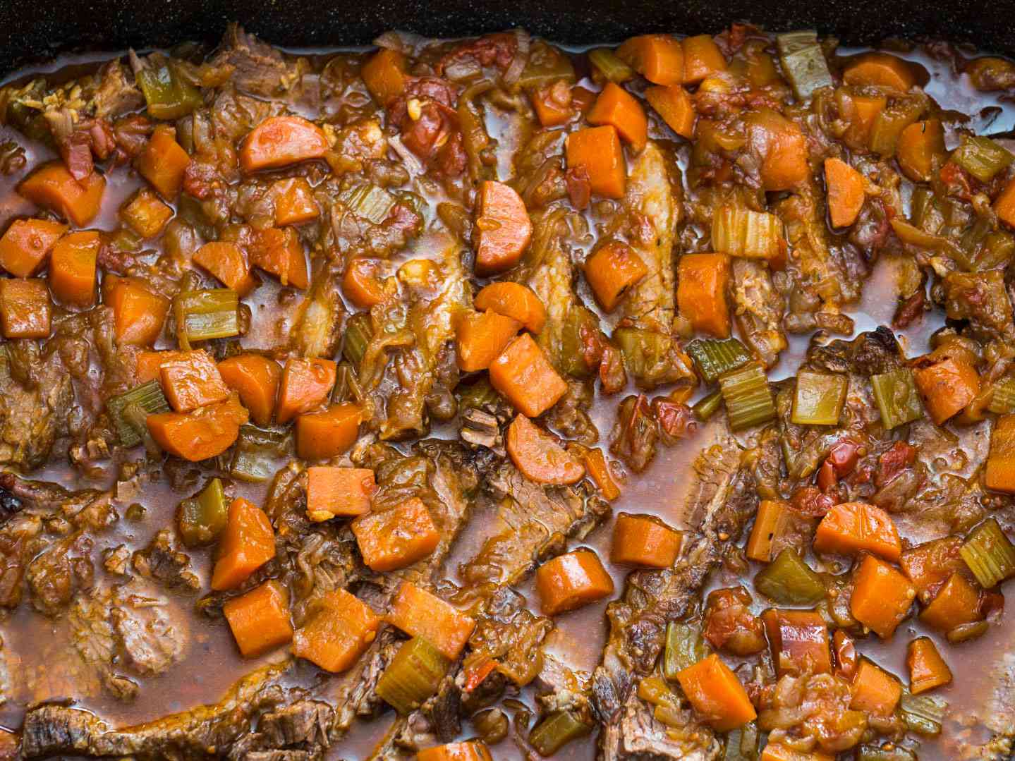 Overhead shot of Jewish-style braised brisket in a sauce with carrots, onions, and other aromatics