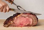 A cooked prime rib roast being carved with a knife and fork on a cutting board