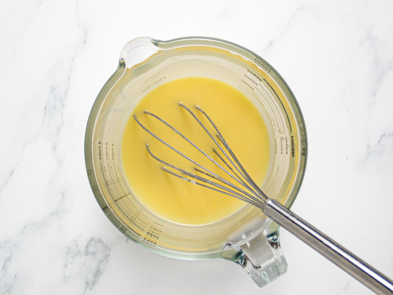 Milk, water, sugar, butter and egg whisked together in a measuring cup, with whisk in it. 