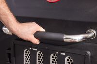 A hand on the handle of a charcoal grill