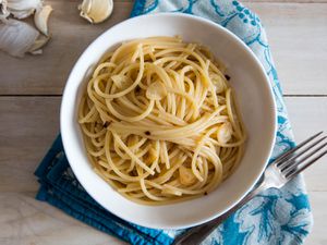 overhead shot of a bowl of pasta aglio e olio, garlic cloves in the background