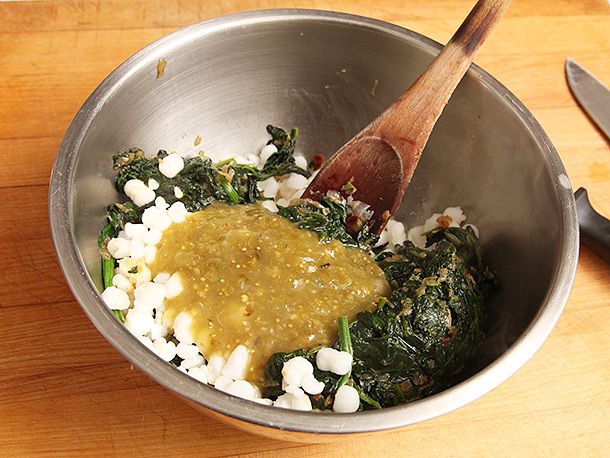 The drained spinach mixture is added to a mixing bowl, along with drained hominy and salsa verde.