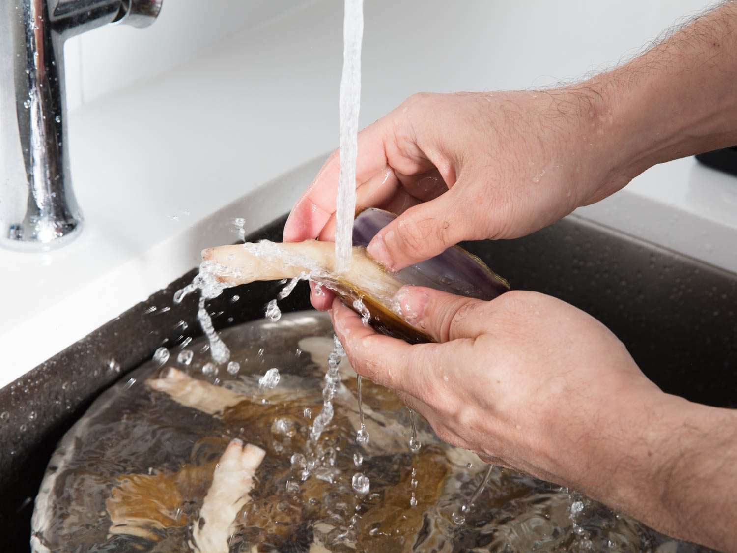 Rinsing off razor clams in running water, with a metal bowl of razor clams below.