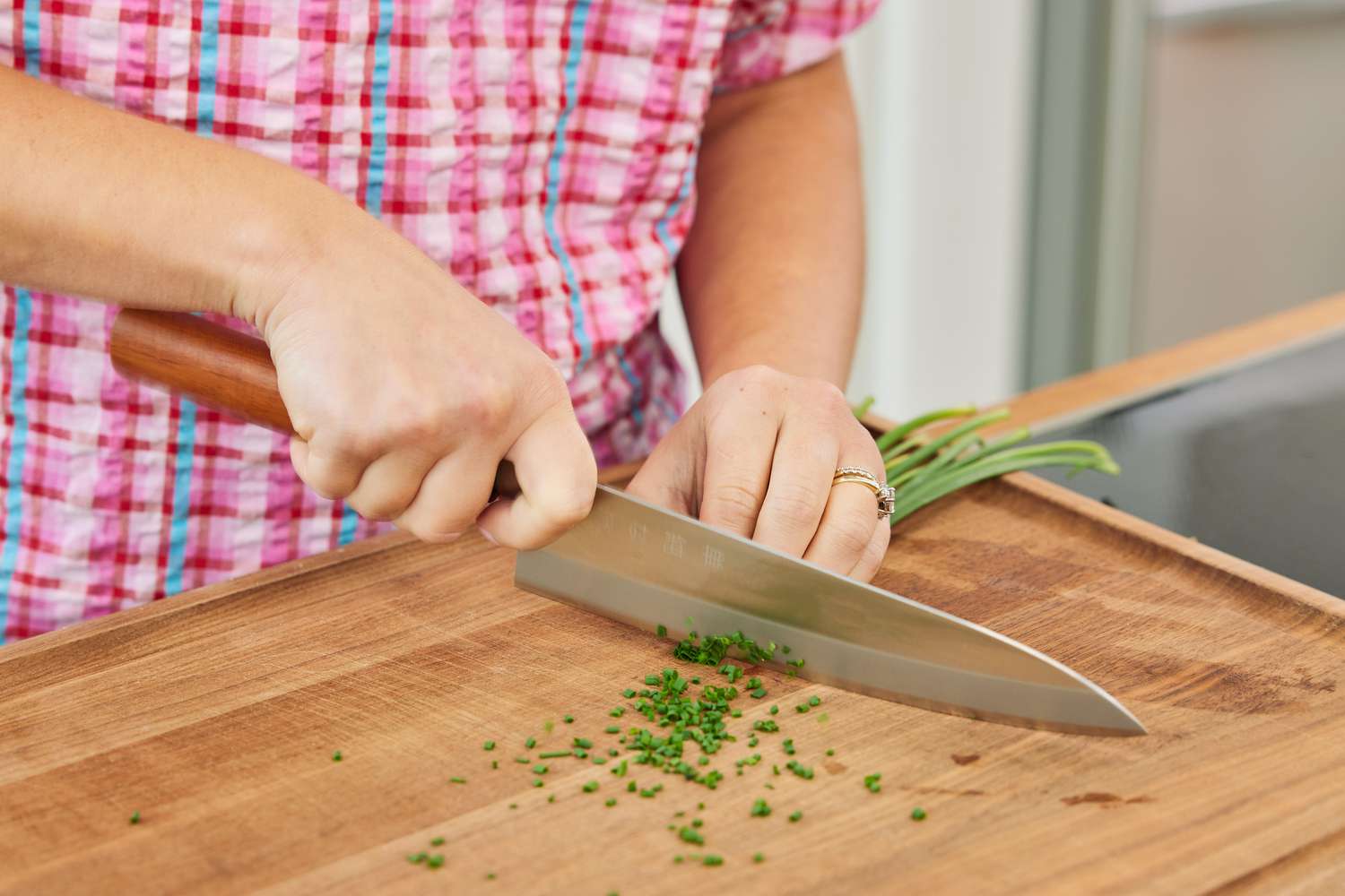 A person using a chef's knife to mince chives on a wooden cutting board