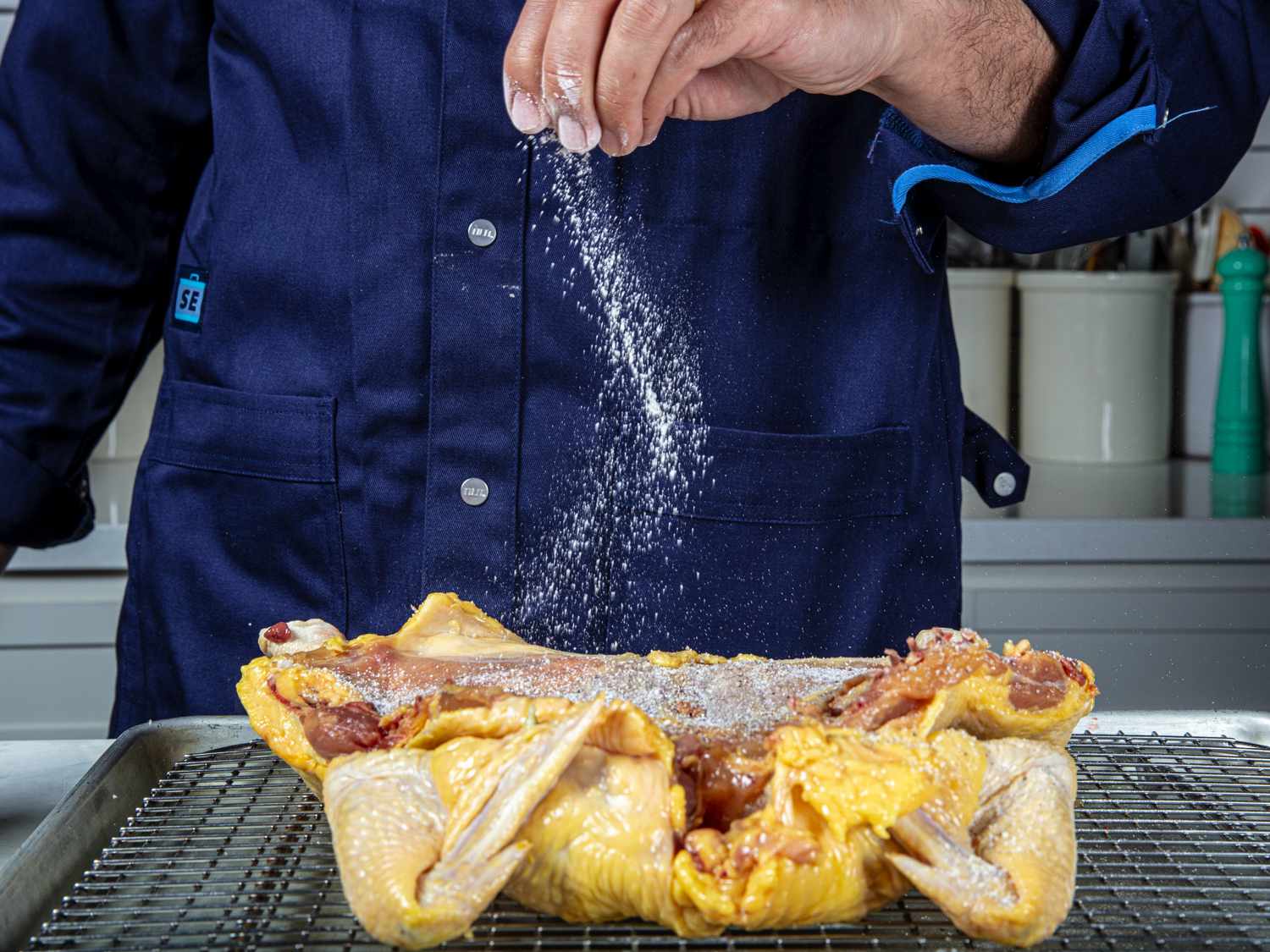 The splayed cavity of a spatchcocked chicken being salted