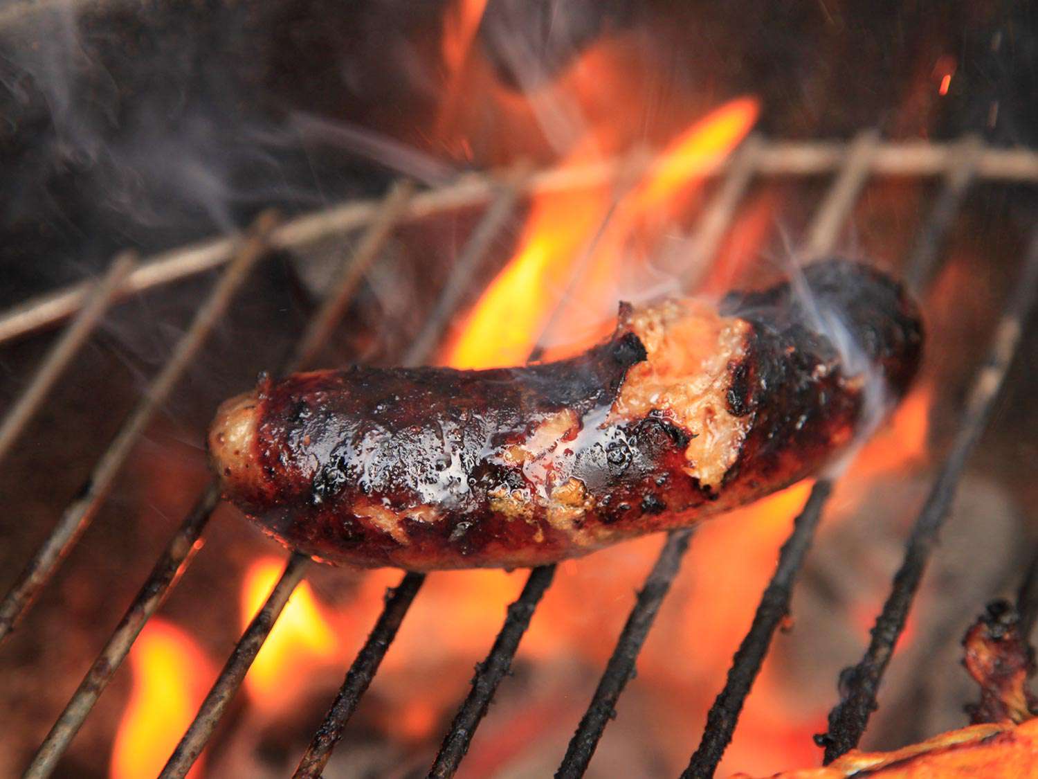 A sausage with a lot of char on a flaming grill.