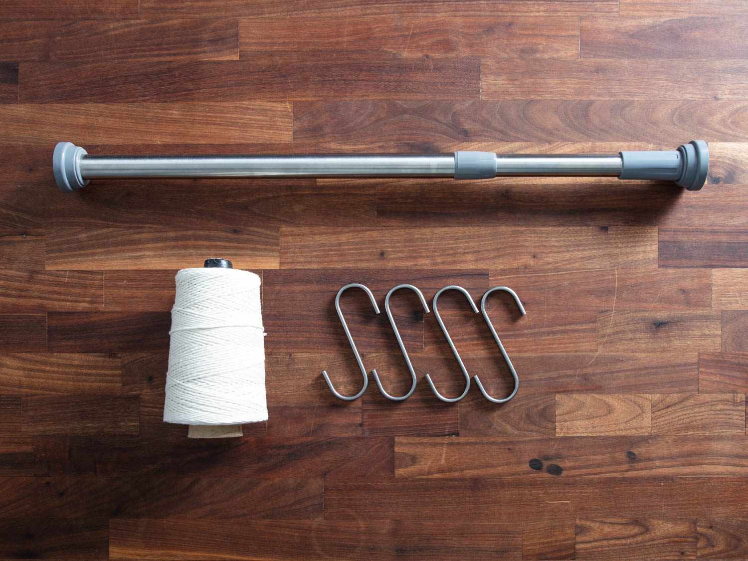 Overhead of equipment for hanging ducks to dry-age in a home fridge: a curtain tension rod, metal S-hooks and butcher's twine.