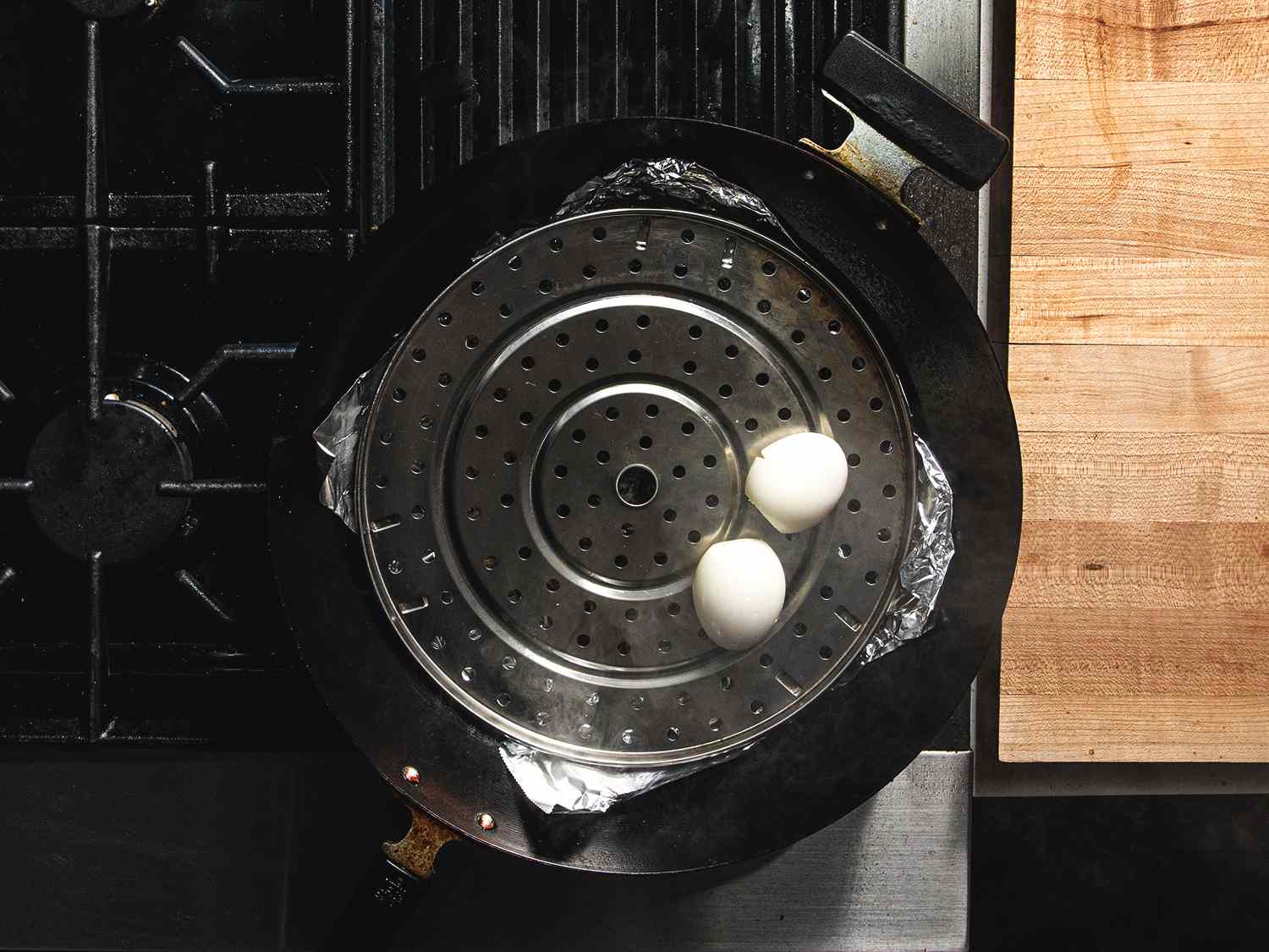 Overhead view of two eggs sitting on a perforated rack in a tin foil-lined wok, ready to be smoked.