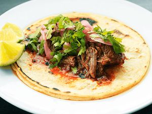 Barbacoa served on a taco made with two corn tortillas on a plate with pickled onions, cilantro, and a lime wedge 