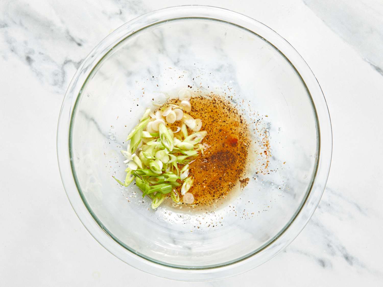 A glass bowl containing sliced green onions oil and seasoning mix