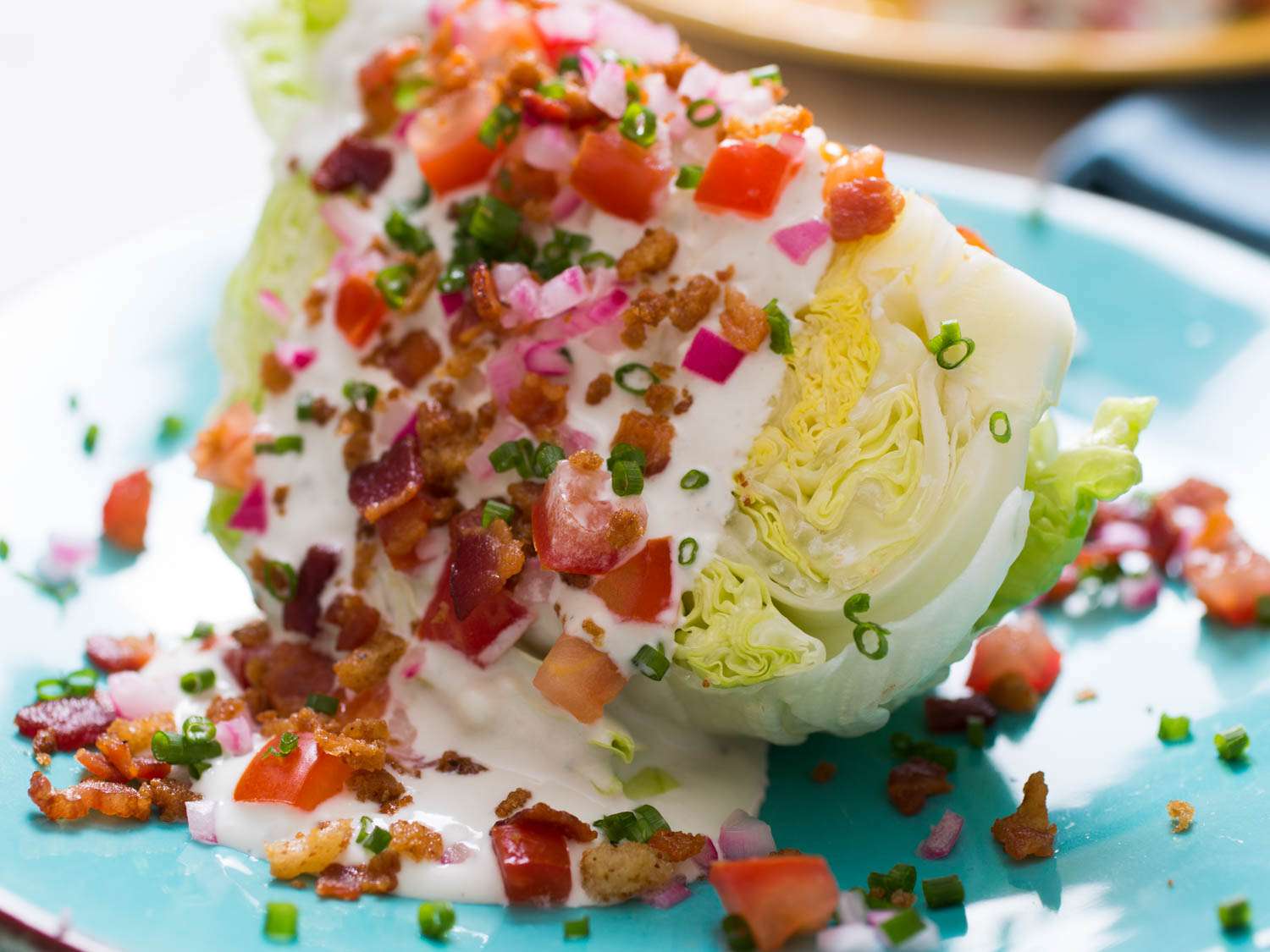 A wedge salad toped with bacon bits, blue cheese dressing, tomatoes, and onions.