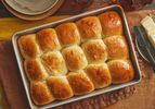 Tray of Parkerhouse Rolls, on a brown textile, with a side dish of butter and small serving dishes to the side. 