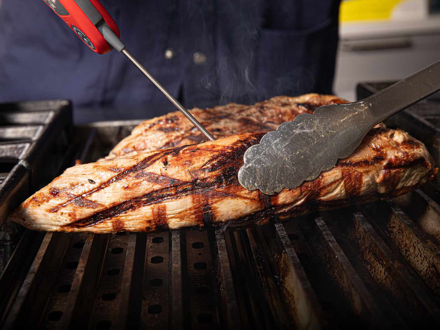 A thermometer is inserted into a pork tenderloin on the grill to check its temperature