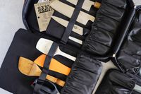 A knife and utensil storage case with various knives a spatula and a wooden spoon secured inside with straps