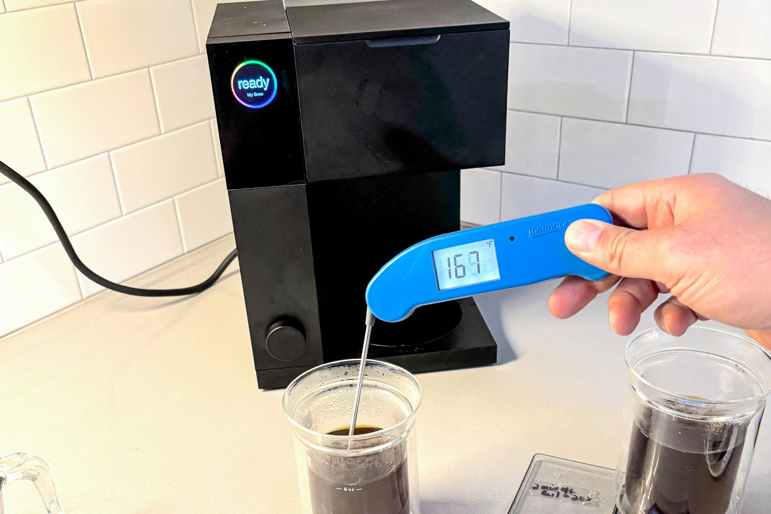 A person taking the temperature of a cup up coffee using an instant-read thermometer.