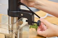 Hands adjusting Anova Culinary Precision Cooker 3.0 attached to a clear container with water